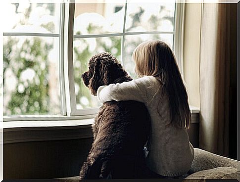 little girl hugging dog in front of the window